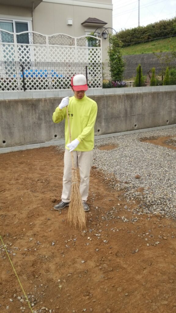 竹ホウキを使って土の表面に残る小さな石までかき集める作業