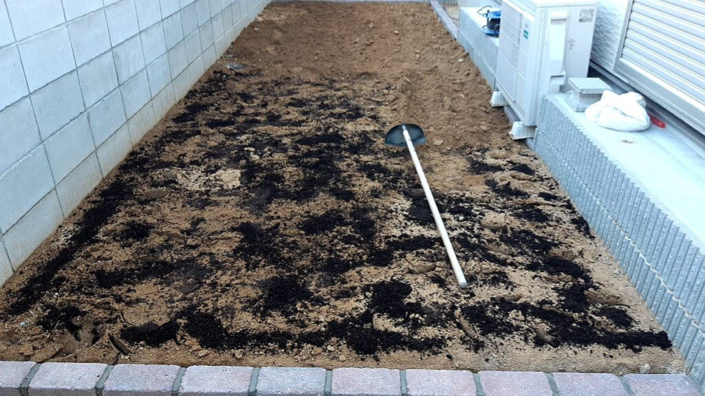 ほぐした土にバーク堆肥をすき込んでいるところ。黒い堆肥が地面いっぱいに広がっている