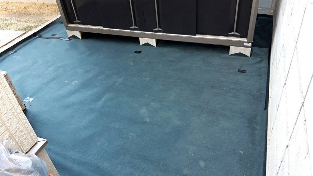 物置の前一面に防草シートを敷き詰めた状態。物置の脚の下までシートが入っている