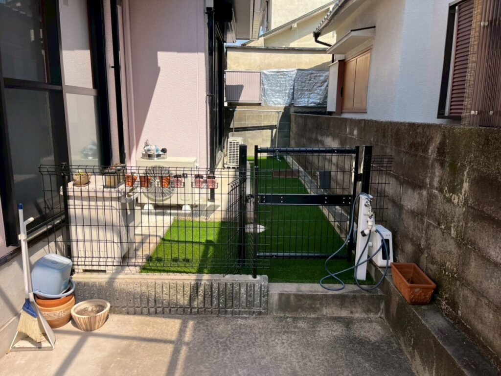 完成後の人工芝通路と黒いフェンス・門扉を、入口側から見通せる完成写真