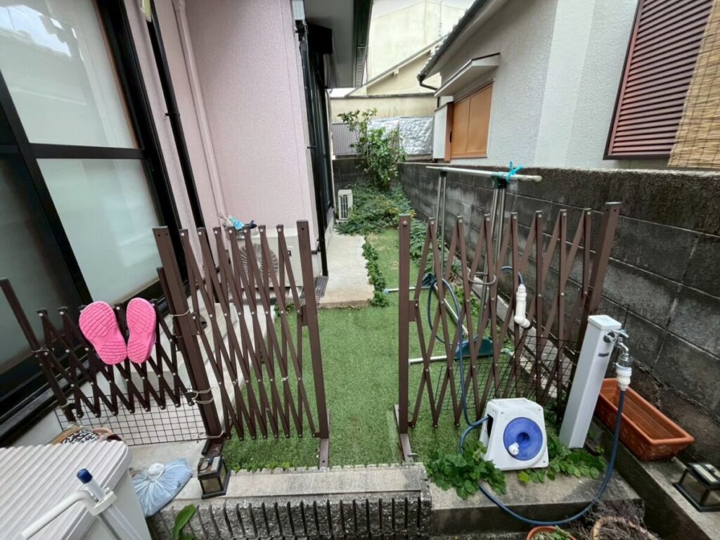 既存の伸縮門扉、室外機、水栓、人工芝が近接している入口側の施工前写真