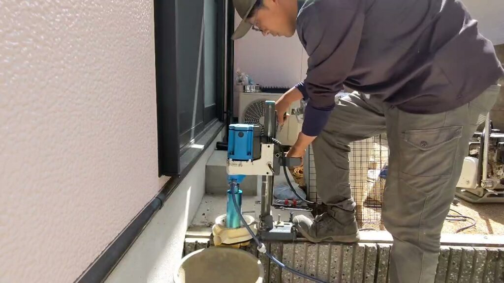既存ブロック塀にコアドリルで穴を開け、黒いフェンス柱を水平器で確認しながら固定している施工中写真