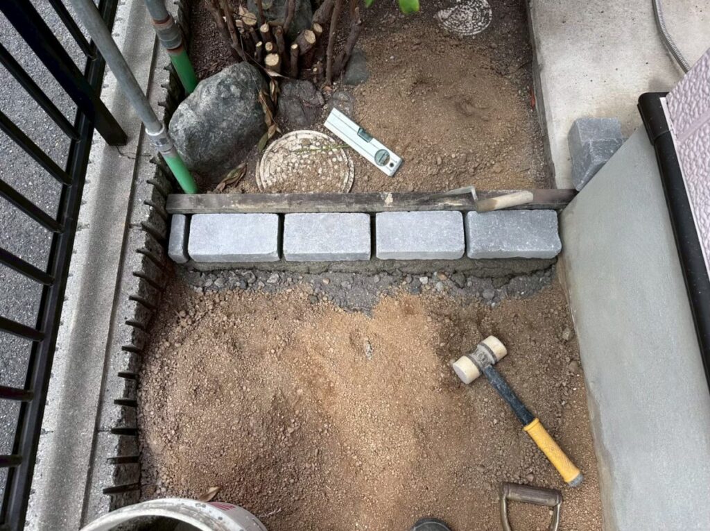 ピンコロ石を境界に沿って並べ、壁際に粒状除草剤を散布している施工中写真