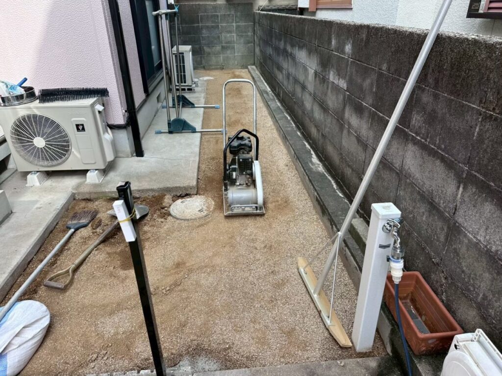 真砂土を通路に搬入し、トンボで敷き均したあと転圧機で締め固めている施工中写真