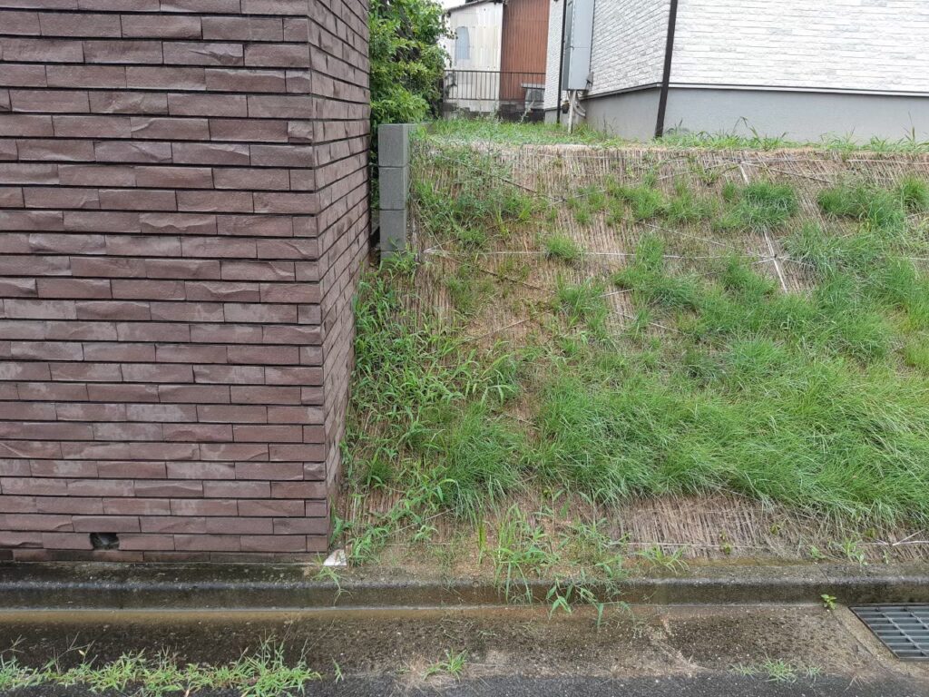 施工前の北西の角。法面の足元がすぐ道路に接し、上に隣家のレンガ塀が建っている