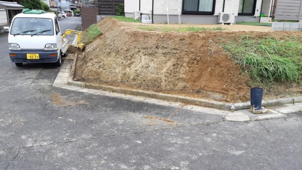ミニユンボで法面の表土ごと草をすき取っているところ。斜面の左半分は土が見え、右半分はまだ草が残っている