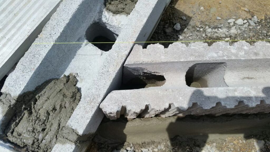目隠しフェンスの基礎ブロックを水糸に合わせて据え、目地にモルタルを詰めているところの寄り