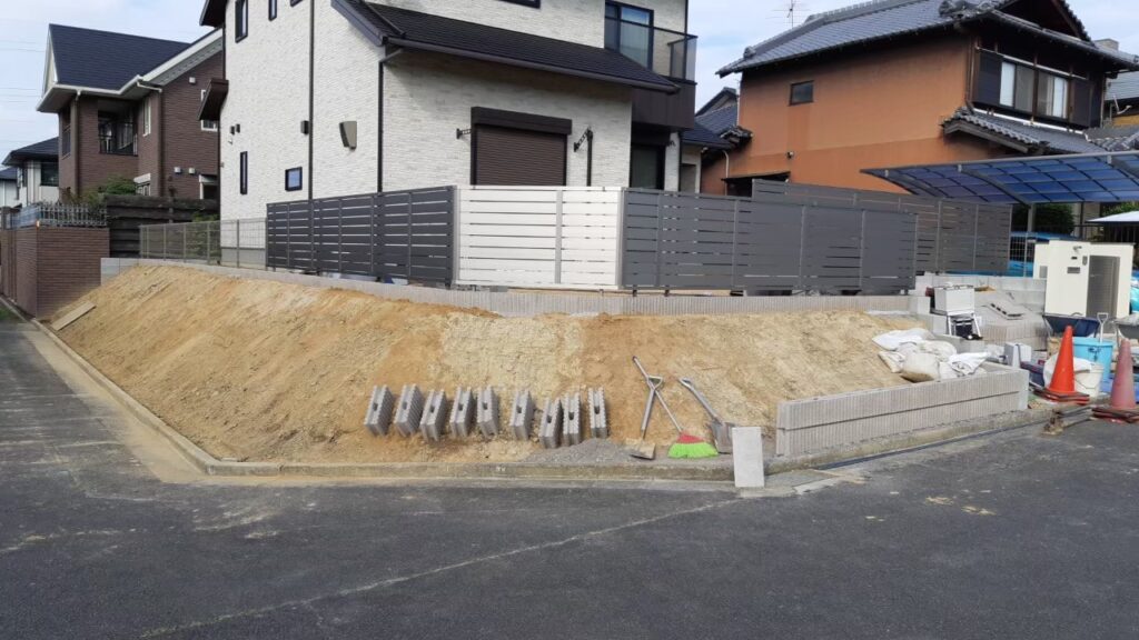 道路から見た施工中の全景。法面上部の目隠しフェンスは完成し、下の斜面はまだ土のまま