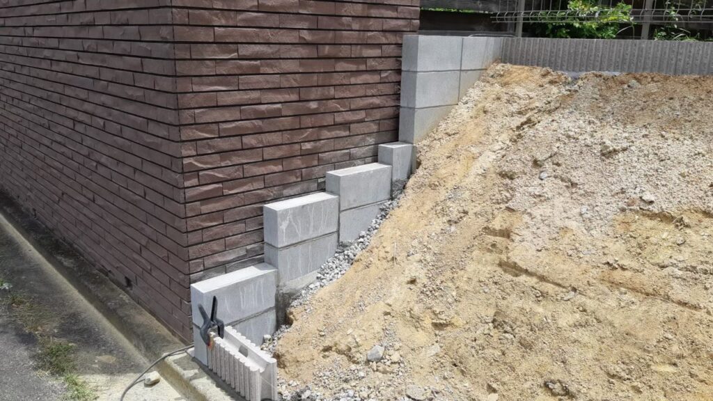 隣家のレンガ塀に沿って、法面の土を止めるブロックを段々に積んでいるところ