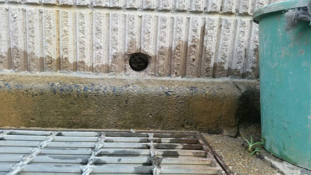 土留めブロックにコアドリルで開けた排水用の丸い穴を道路側から見たところ。すぐ下に側溝のグレーチング
