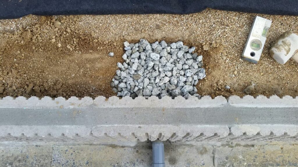 土留めブロックを貫通させた排水管と、水が抜けるように管のまわりに入れた砕石