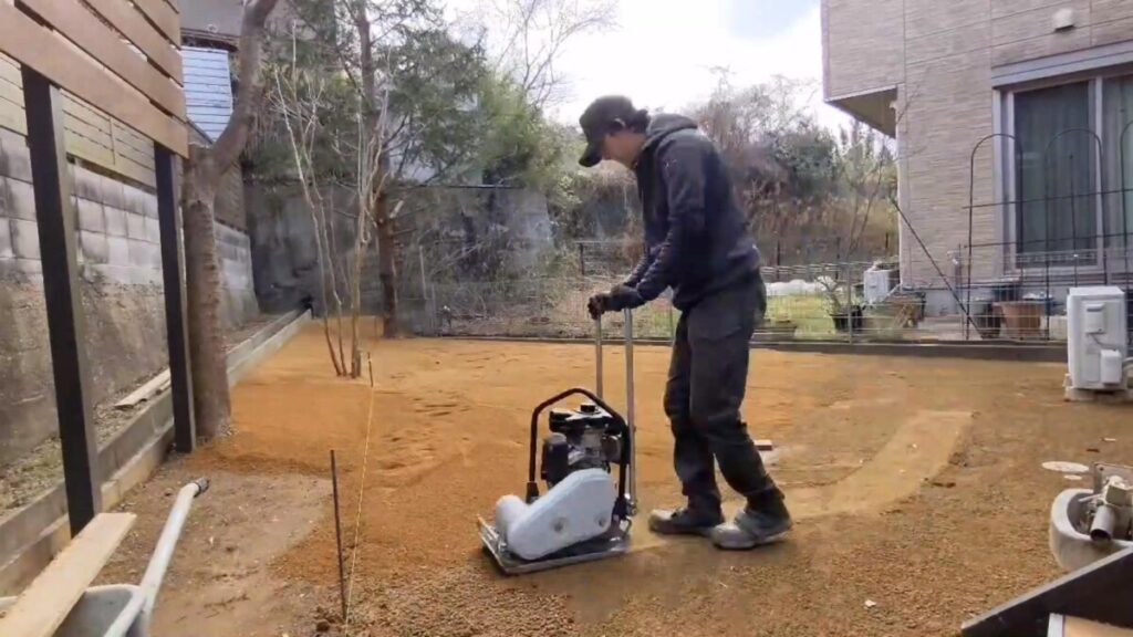 プレートコンパクターを走行させ、むき出しになったお庭の土の表面をフラットに締め固めている転圧シーン